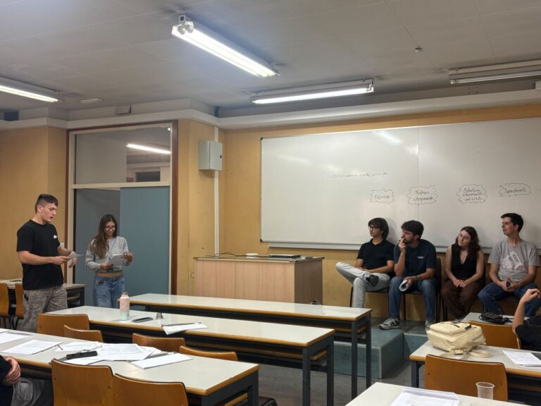 Varios estudiantes leen un caso práctico de pie mientras otros escuchan sentados delante de la pizarra.